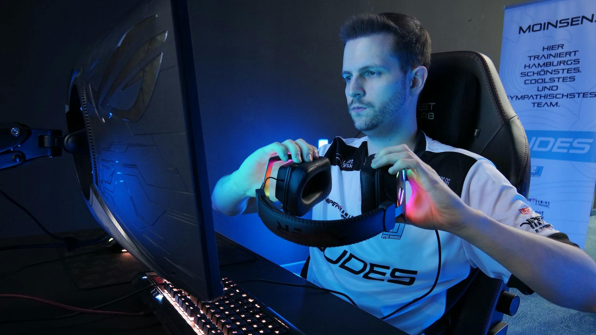 An esports player sits in front of his gaming setup and puts his headphones on