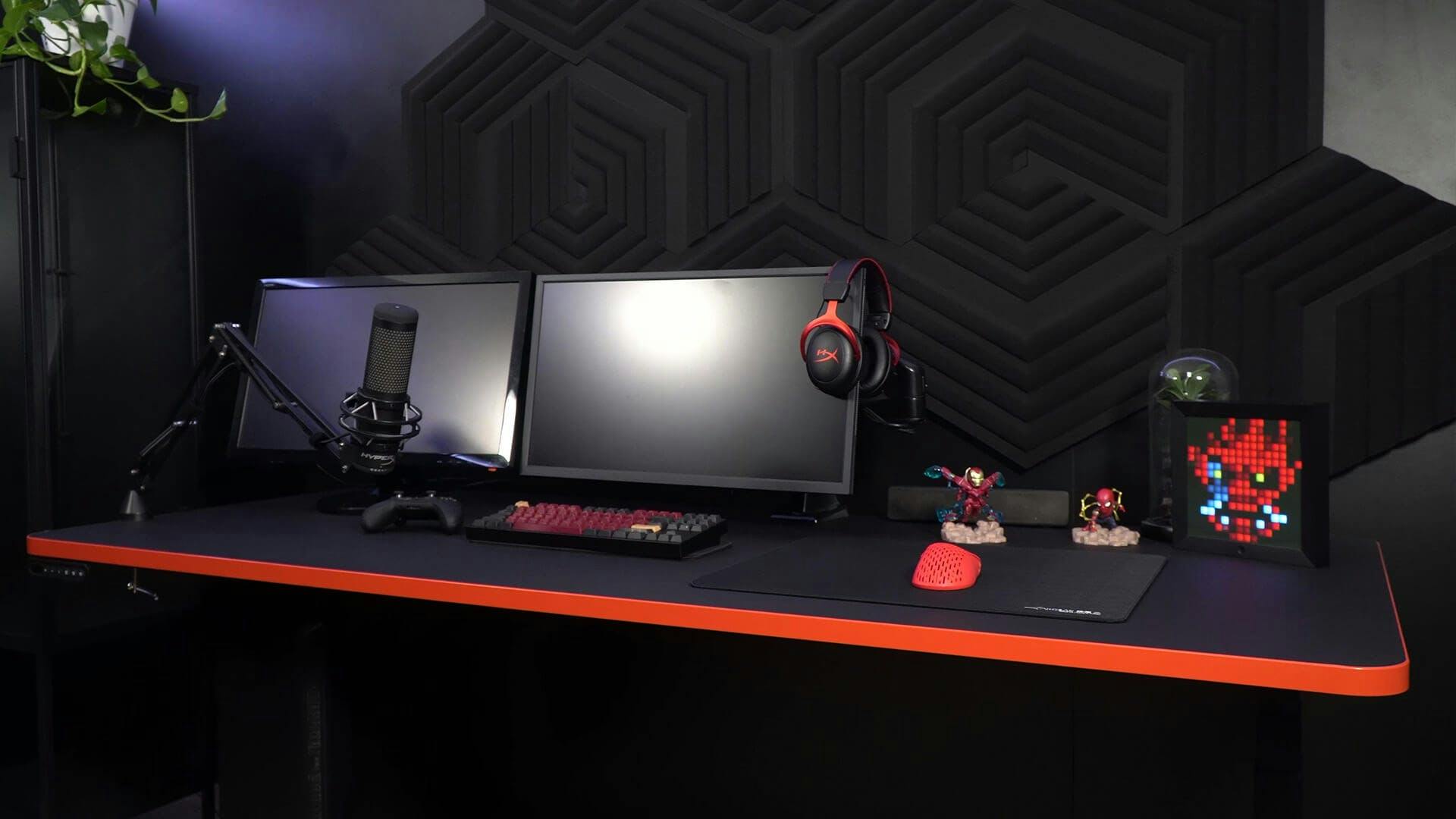 Auf einem Gaming Tisch von LeetDesk steht nur wenig Gaming Dekoration zwischen dem essentiellen Gaming Setup Zubehör wie Monitoren, Tastatur und Mikrofon